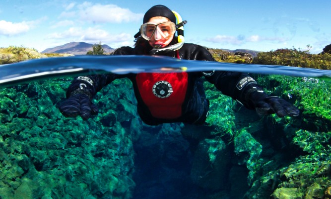 Underwater half-and-half shot of snorkeler between the continental plates in Silfra fissure on sunny day